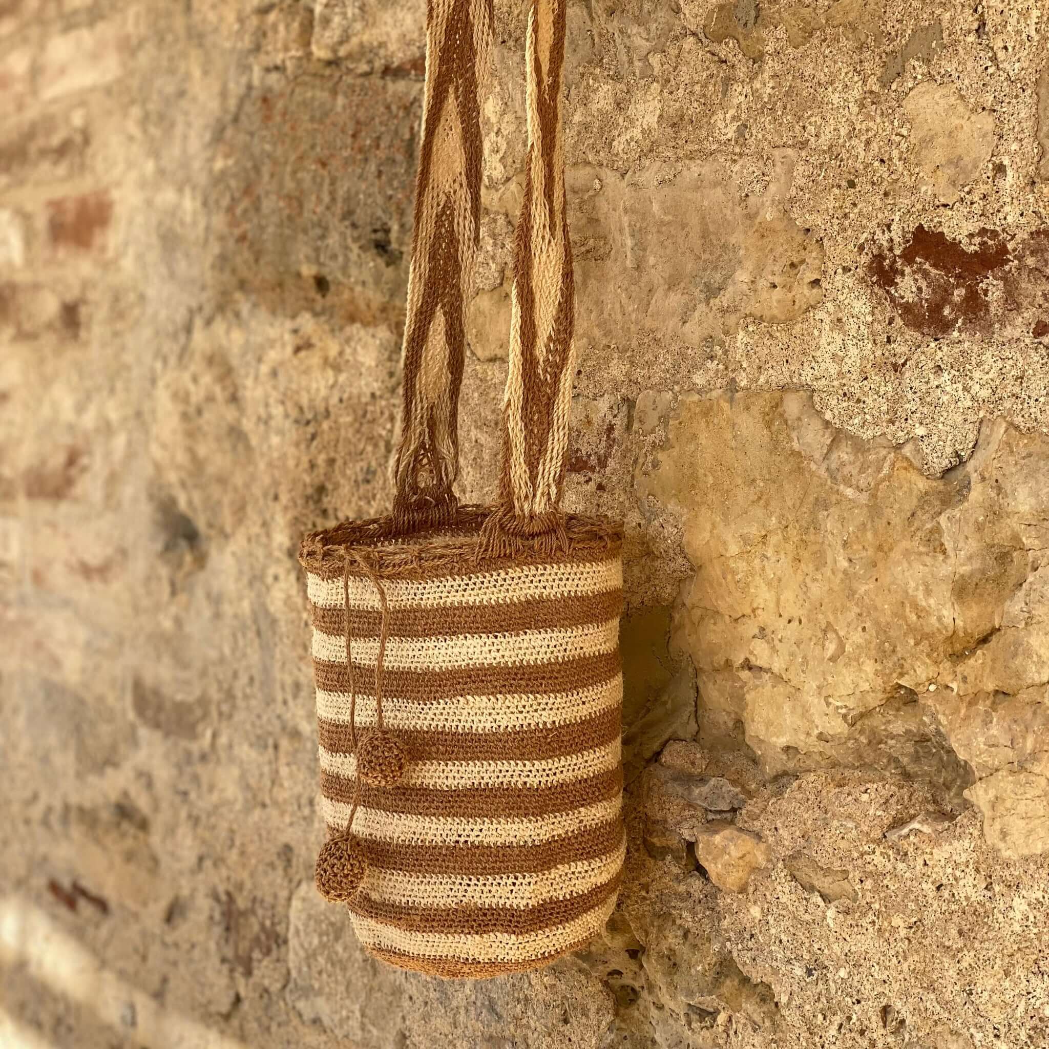 Borsa artigianale a righe beige e avorio appesa a un ramo, intrecciata a mano in fibra naturale fique