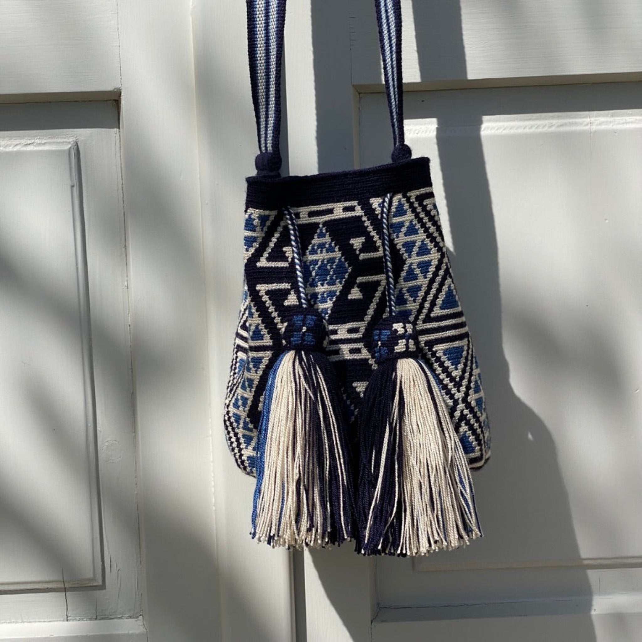 Borsa Wayuu blu e avorio, realizzata a mano in Colombia, fotografata appesa con luce morbida – Volver Bags