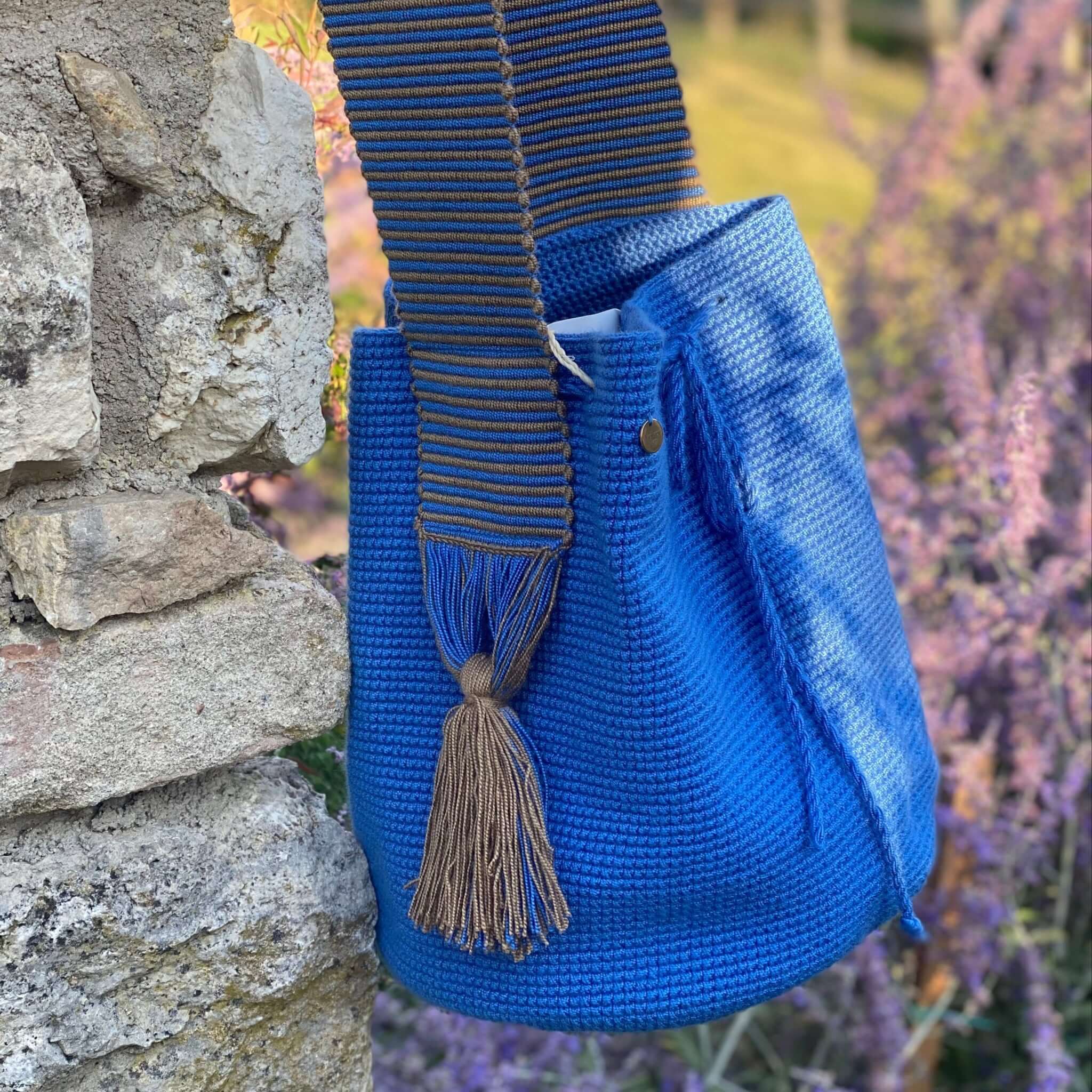 borsa wayuu blu cobalto con dettaglio della tracolla e nappine laterali appesa ad un muretto con lavanda sullo sfondo