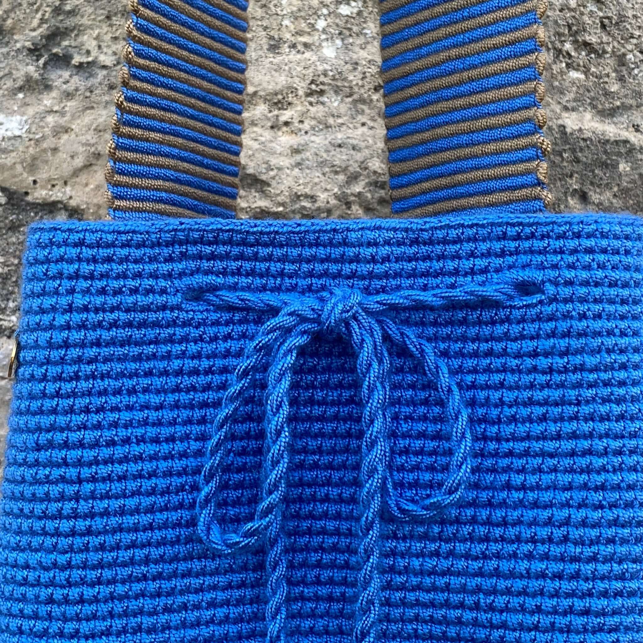 dettaglio macro del fiocco e della particolare lavorazione intricata della tracolla nei colori blu e grigio e della della borsa artigianale blu cobalto realizzata a mano all'uncinetto