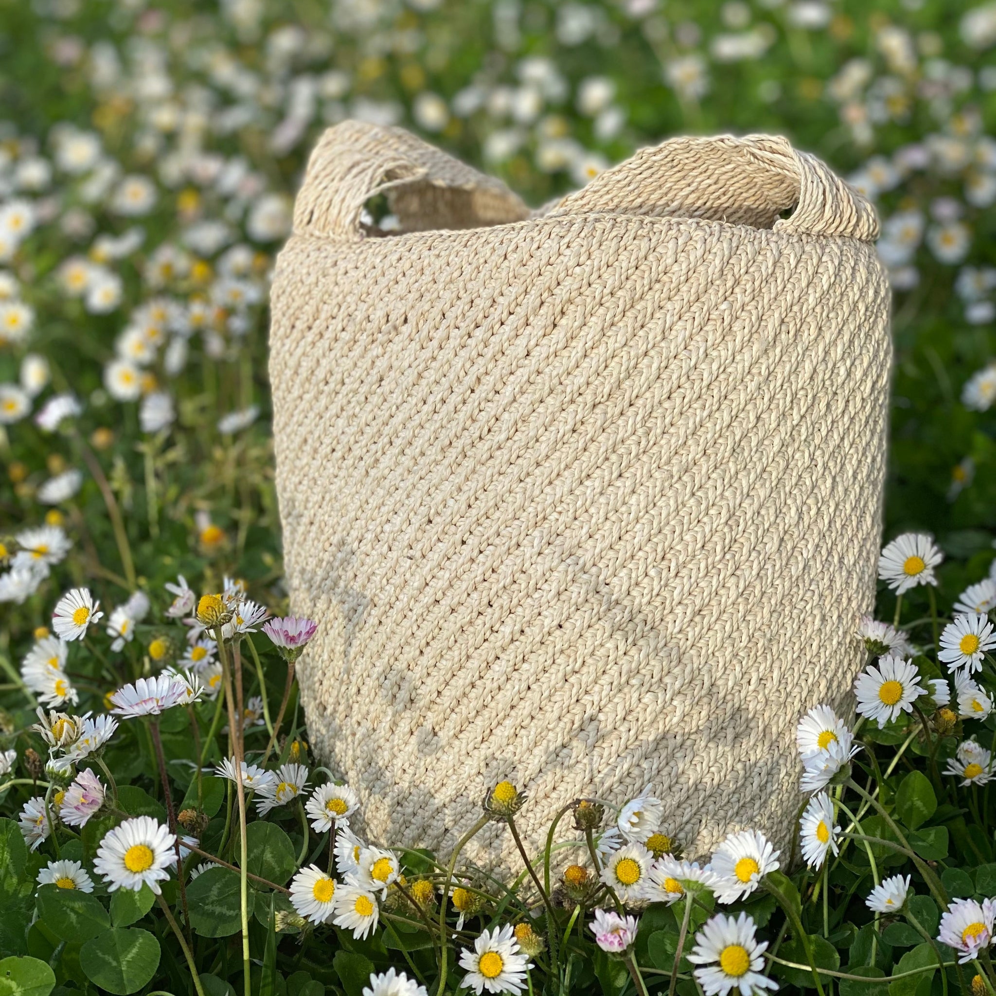 Borsa Leticia Volver Bags, lavorazione etica in palma chambira dell’Amazzonia colombiana, borsa appoggiata su un letto di margherite che ne contrastano il colore bianco ecru