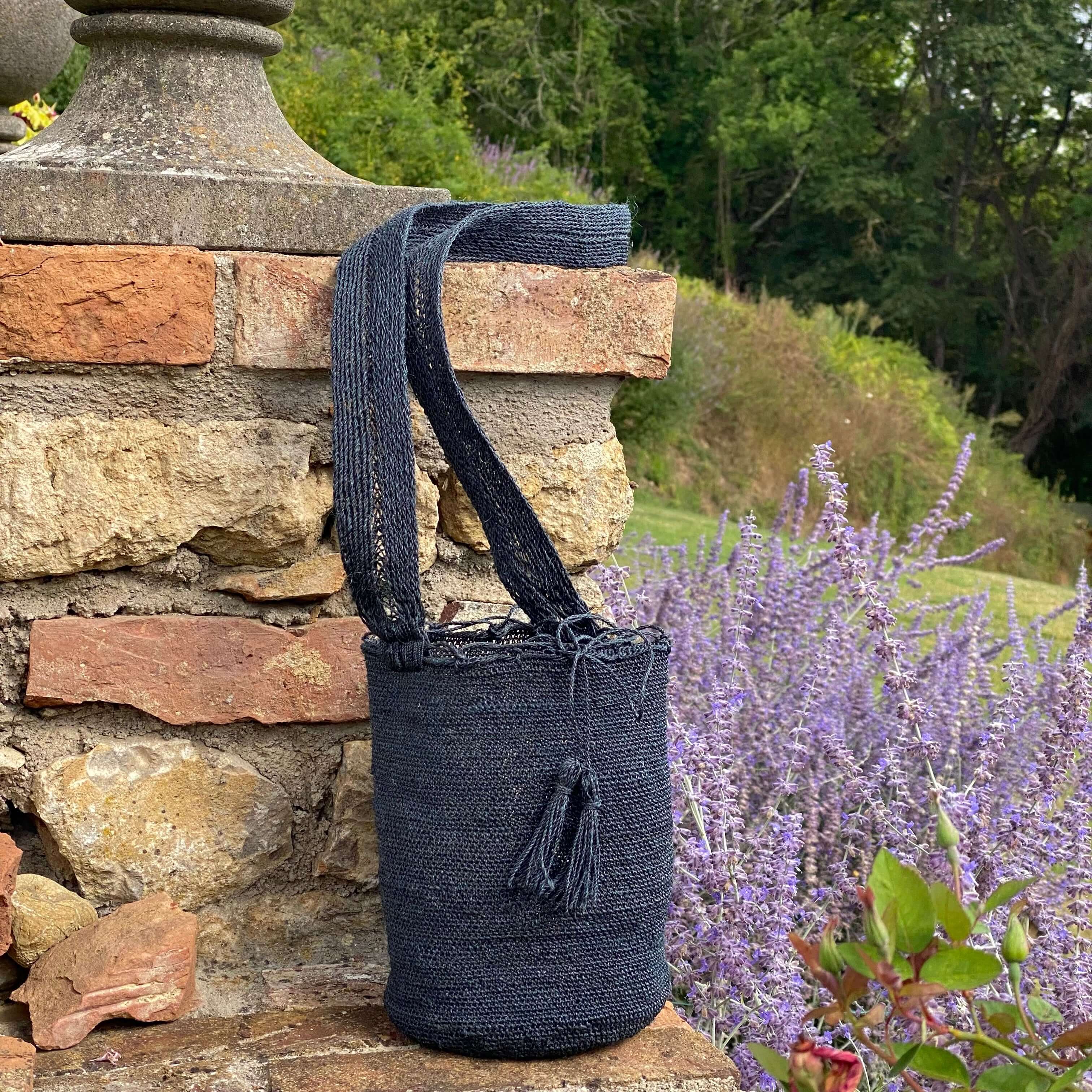 borsa in fibra naturale fotografata in esterno su un muretto rustico e fiori di lavanda. Dalla foto si può apprezzare l 'artigianalità della borsa e la texuture materica. Si percepisce la leggerezza della borsa nella trama intricata