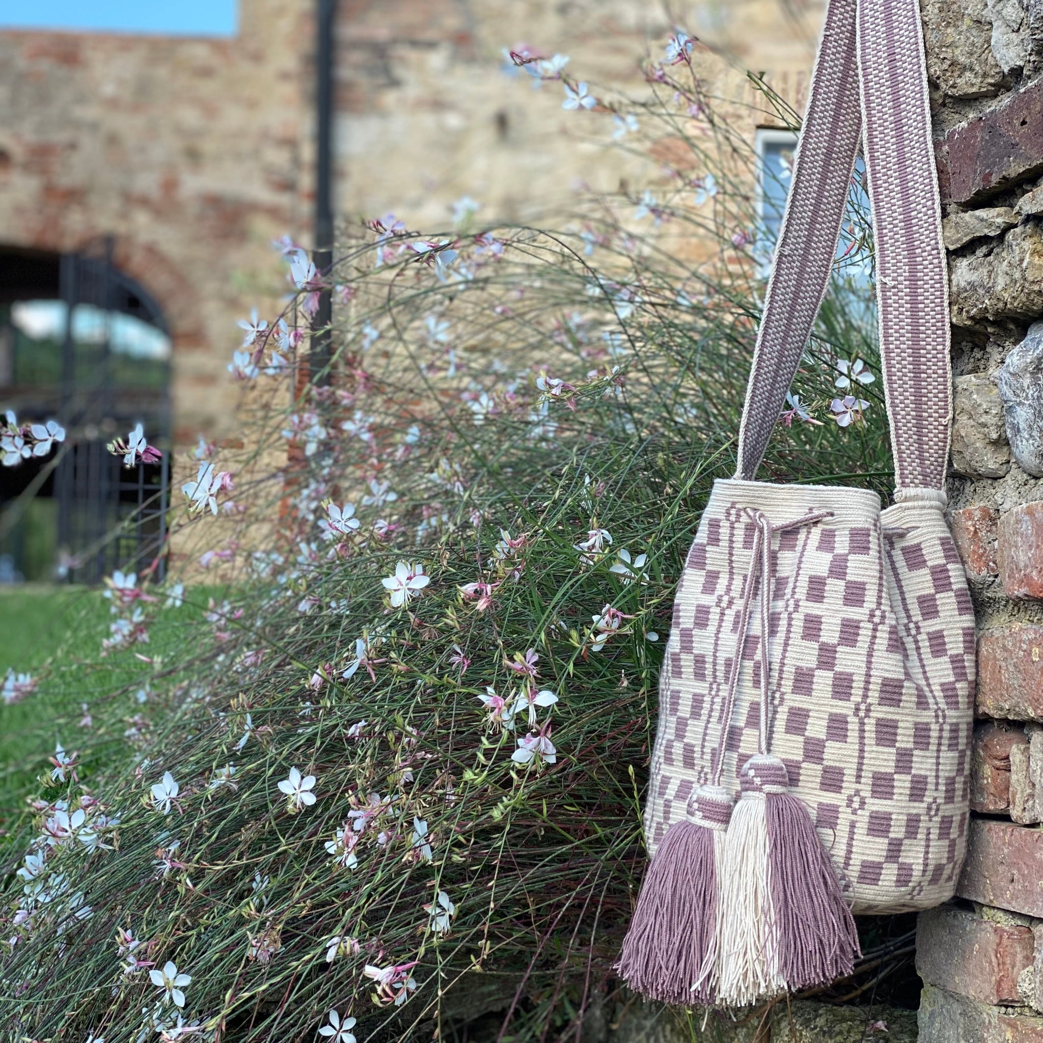 borsa artigianale wayuu originale, dettagli geometrici e nappe su fondo floreale di un casale toscano volver bags