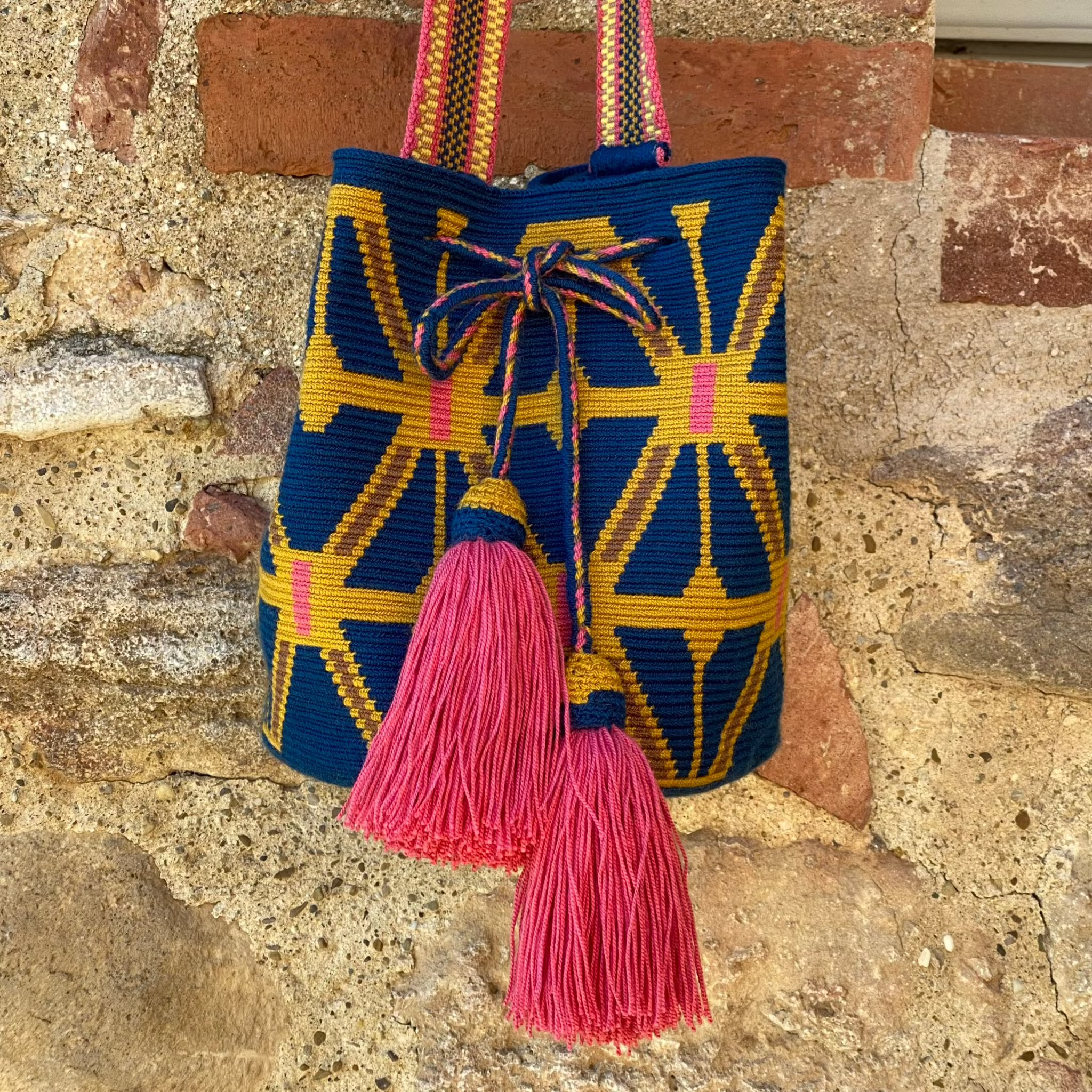 Mochila Wayuu intrecciata a mano con motivi geometrici gialli su base blu e nappine fucsia – Volver Bags