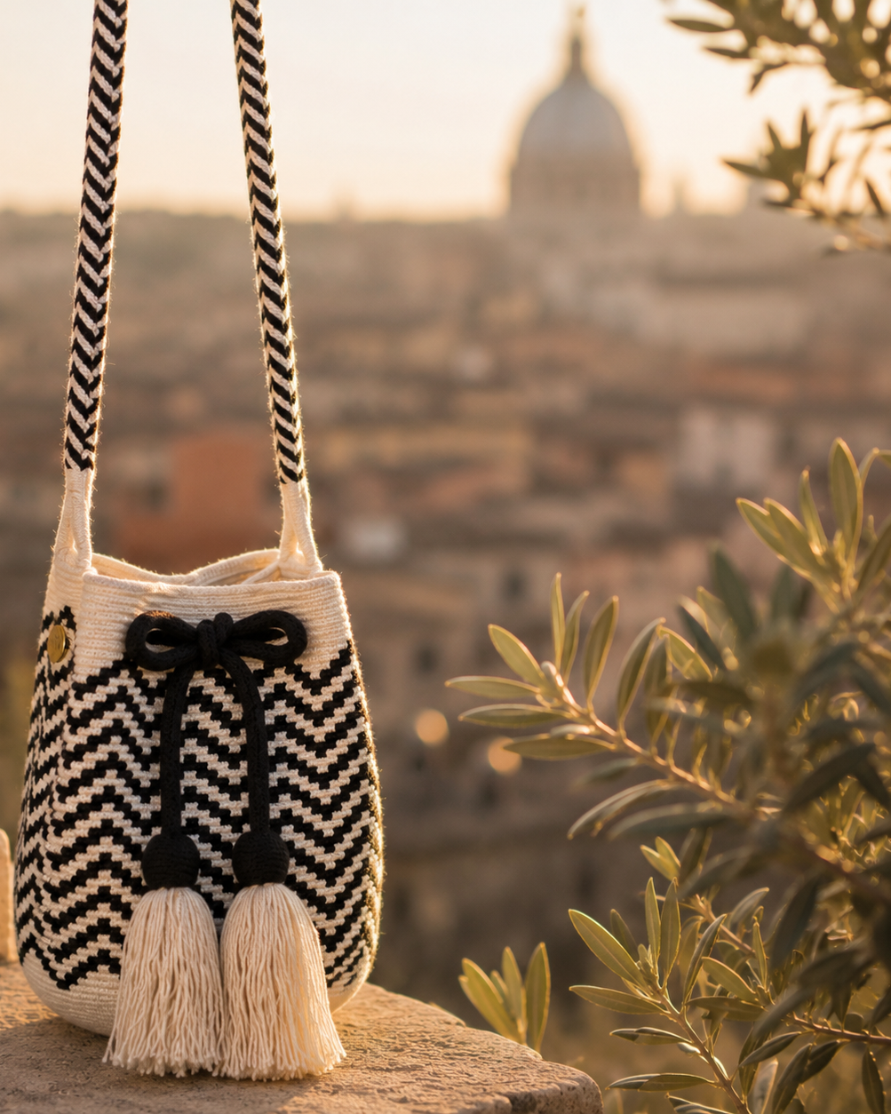 borsa intrecciata a amano bianca e nera con nappine rifinite con sfondo di roma antica al tramonto