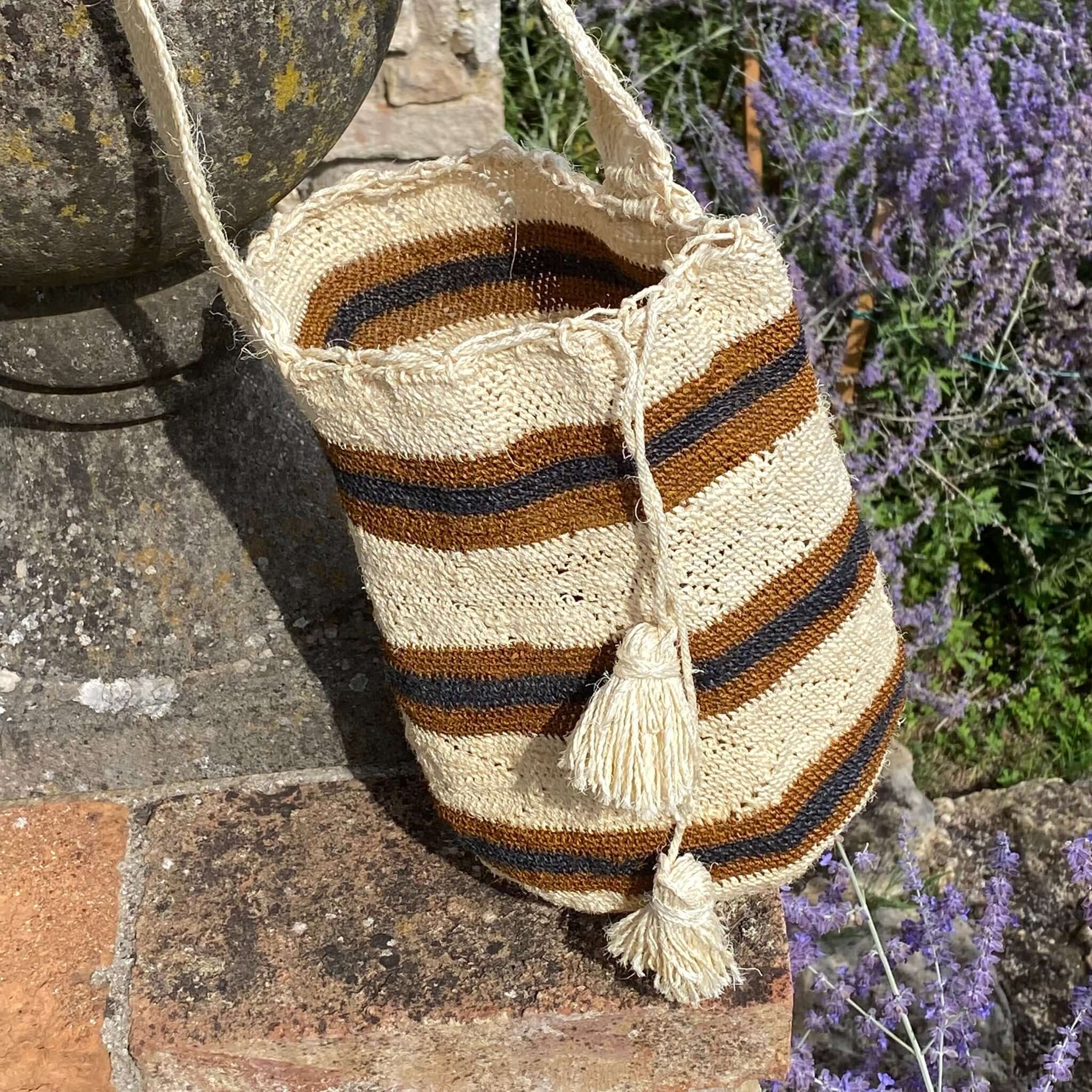 Dettaglio della FIBI Bag Tatacoa in fibra naturale di fique intrecciata a mano, con righe orizzontali color ruggine e blu su fondo beige. La texture è ben visibile in luce naturale.