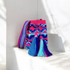  Mochila Buenas: lavorazione a filo singolo, intreccio fucsia e azzurro, simbolo dell’artigianato autentico Wayuu. Nappine rifinite e tracolla tessuta sl telaio a mano