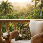 Borsa esclusiva Wayuu. artigianato colombiano con stile italiano. in beige e crema con motivi geometrici e grandi nappine, fotografata su un muretto di pietra davanti a una villa d’epoca con giardino all’inglese e fontana.
