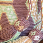 Borsa artigianale Wayuu elegante con nappine decorative e tracolla intrecciata nei toni malva, beige e verde chiaro.