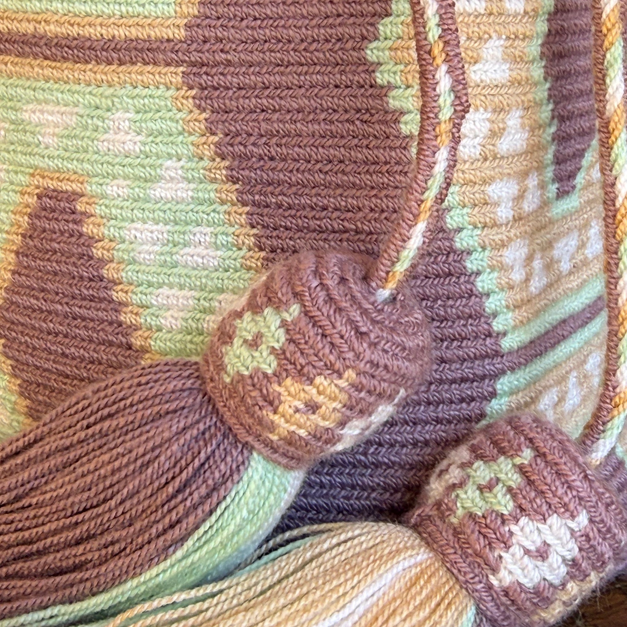 Borsa artigianale Wayuu elegante con nappine decorative e tracolla intrecciata nei toni malva, beige e verde chiaro.