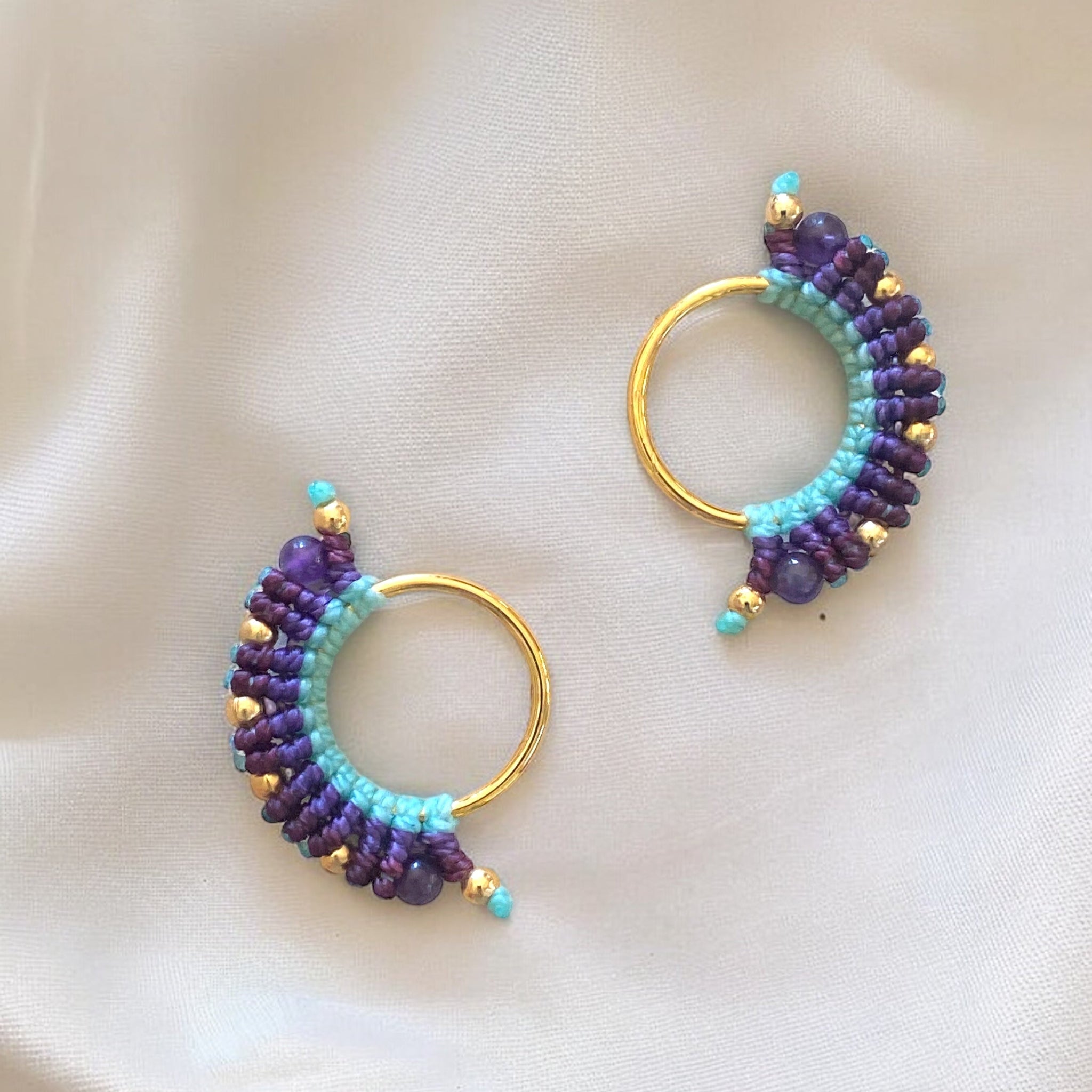 Orecchino macramè in primo piano con fili di cotone azzurri e due sfumature di viola, lavorato a mano e rifinito con base dorata