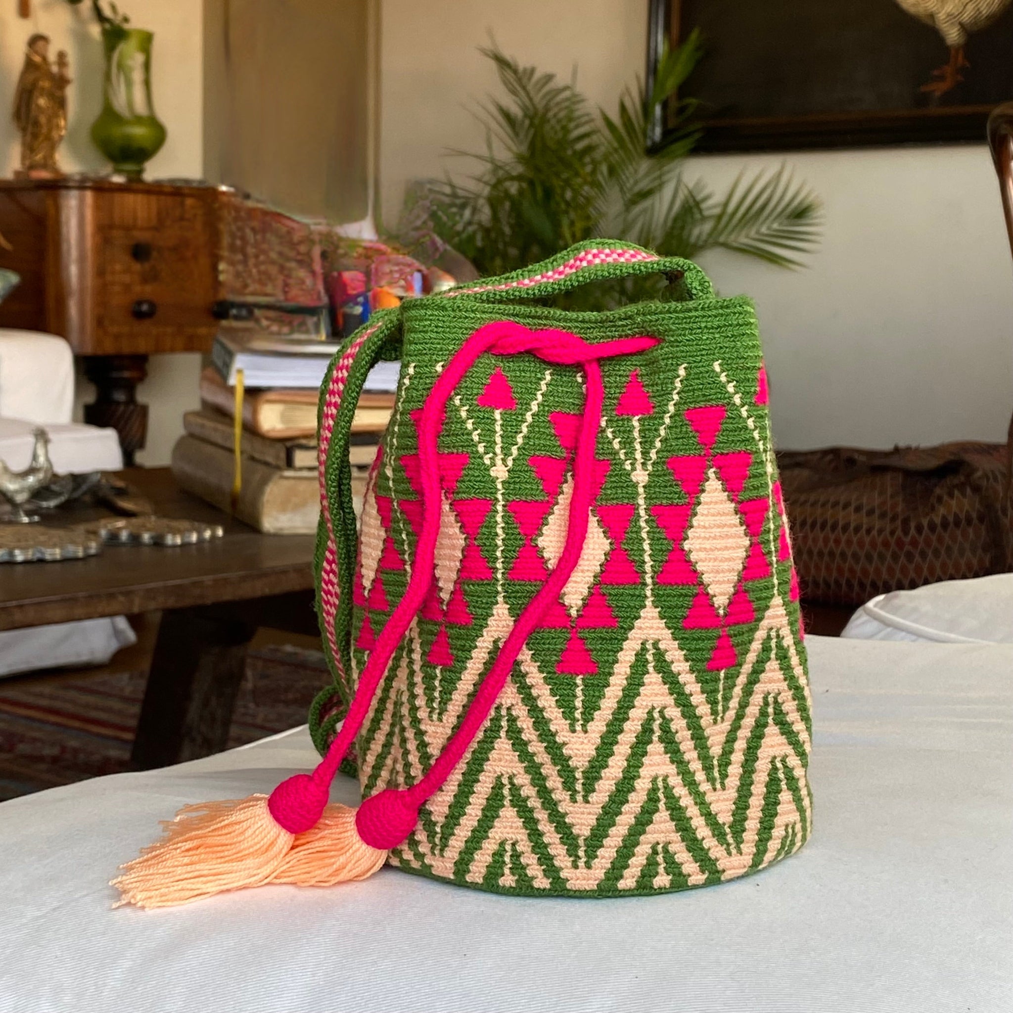 Borsa artigianale Wayuu su sfondo indoor, decorata con motivi geometrici tradizionali e nappine color pesca
